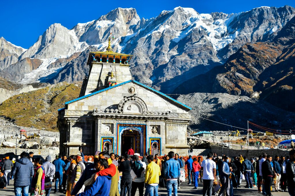 Crowd gathers at Kedarnath Temple with Himalayas backdrop, showcasing religious significance and stunning landscape.